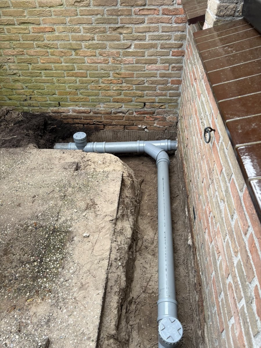 Nieuwe PVC-leiding met ontstoppingsstuk langs een gevel